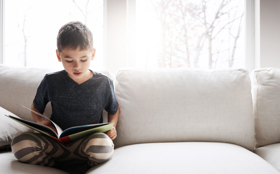 Boy reading a book while relaxing on the sofa at home.
