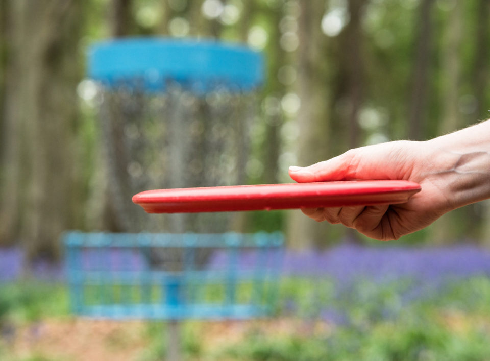 Close-up of a woman's hand as she throws a carefully aimed frisbee disc toward the basket.