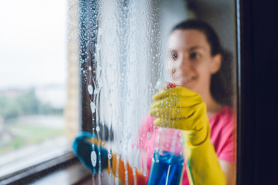 Young woman wiping windows at home