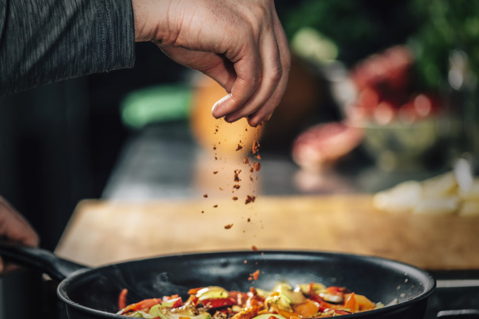 Sprinkling ground red chili pepper paprika over sliced vegetables,