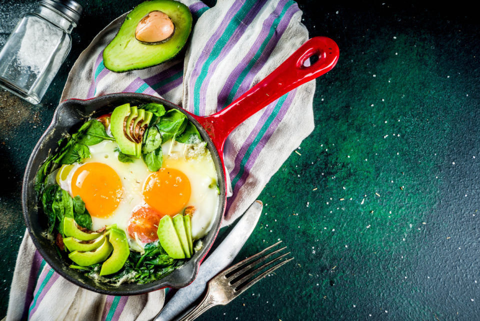 Green vegetable shakshuka. Middle eastern traditional dish shakshouka. Fried eggs with tomatoes, baby spinach, vegetables and herbs, Dark green background top view.