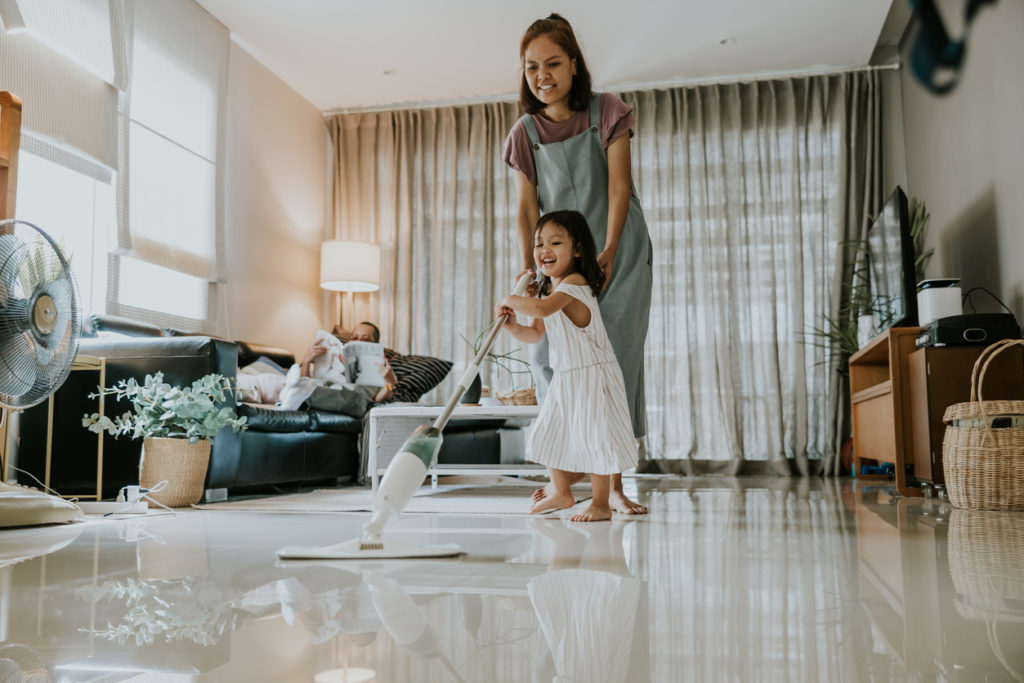 Cute toddler girl helping her mom cleaning the floor with mop.