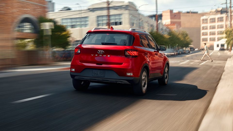Rear view of a red 2020 Hyundai Venue driving down a city street