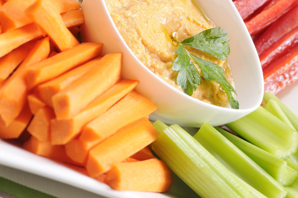 Close-up of a plate of fresh veggies with red pepper hummus for dip.