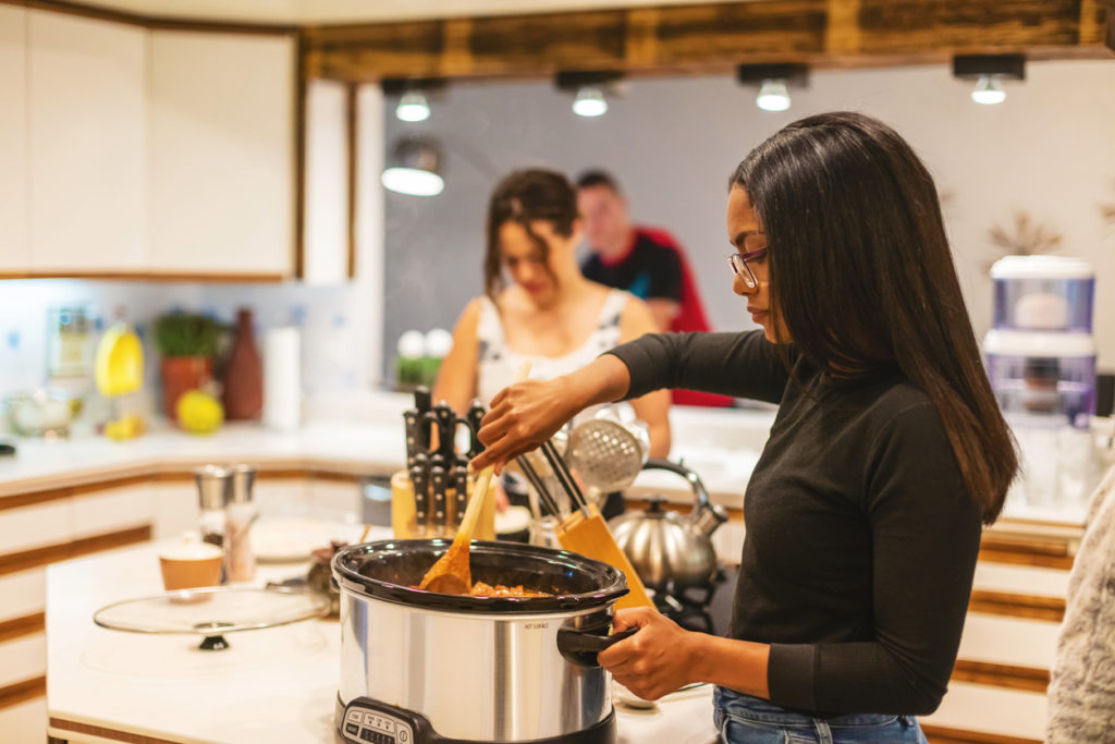 Group of young adults cooking together in the kitchen and using a crockpot