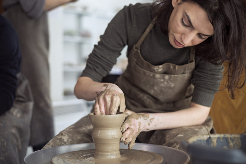 Young woman artist making clay bowl on pottery wheel